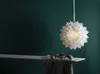 A white paper star lantern hangs in front of a dark green wall, with a wooden shelf and draped fabric in the foreground. Podgląd zdjęcia produktu