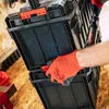 A person wearing orange gloves is holding a black tool case. Náhled obrázku produktu