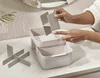 A person's hands are shown cleaning a modular cosmetic organizer on a countertop. Náhled obrázku produktu