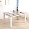 A dining table is shown in a room with light wood flooring and a window with blue curtains in the background. There are two framed pictures on the wall. Produktbild-Vorschau