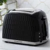 A black Russell Hobbs toaster with a textured surface, sitting on a marble countertop with a decorative gold and white tiled backsplash in the background. Náhled obrázku produktu
