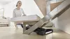A woman is cleaning under a staircase with a cordless vacuum cleaner. Produktbild-Vorschau