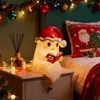 A cute ghost-shaped night light wearing a Santa hat and reading a book sits on a bedside table next to a diffuser and Christmas lights. Produktbild-Vorschau