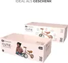 Two pink boxes of a Kinderkraft CUTIE mini balance bike are shown, one in the foreground and one slightly behind and to the right. The box in the foreground features an image of a child on the bike. Voir les images du produit