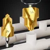 Two gold drill bits are shown in front of white pipes, with one drill bit being used by a drill. Náhled obrázku produktu