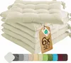 A stack of cream-colored seat cushions with ties, a tag indicating a set of 6, and a row of color swatches at the bottom. Produktbild-Vorschau