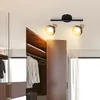 A ceiling light fixture with two adjustable spotlights is mounted on a ceiling above an open closet with clothes hanging inside. Voir les images du produit