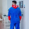 A man wearing a Spiderman costume stands in a room with a desk and pictures on the wall. Anteprima dell’immagine prodotto