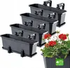 A set of four dark gray balcony planters with attached hangers, arranged in a staggered formation. One planter in the foreground is filled with red and white flowers. Podgląd zdjęcia produktu