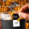 A hand is placing a label on a glass with a textured black base. Náhled obrázku produktu