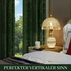 A bedside table with a lamp and candle next to a bed with green curtains in the background. Voir les images du produit