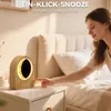 A woman is reaching out to touch a sunrise alarm clock on a nightstand next to a bed. Produktbild-Vorschau