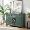 A green sideboard with decorative elements is shown in a room setting with plants and artwork. Produktbild-Vorschau