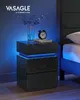 A black LED nightstand with two drawers is shown in a bedroom setting. Náhled obrázku produktu