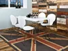 A dining set with white chairs and a white table is placed on a Union Jack rug in a room with a wooden plank wall. Podgląd zdjęcia produktu