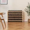 A wooden wine rack filled with wine bottles, placed on a wooden floor next to a chair and a plant. Produktbild-Vorschau