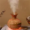 A wooden-style essential oil diffuser emitting mist, placed on a surface with a book. Produktbild-Vorschau