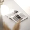 An open magazine on a white surface, with a bright light source creating a glare. Náhled obrázku produktu