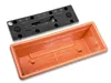 A black plastic lid with a water reservoir mechanism sits above an orange terracotta planter. Anteprima dell’immagine prodotto