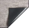 The underside of a rug is shown, with the corner flipped up to reveal the black backing. Voir les images du produit