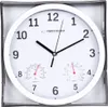 A white analog clock with two smaller dials for temperature and humidity, displayed in its packaging. Produktbild-Vorschau