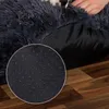 A close-up view of the bottom of a dark gray, plush dog bed, showing the anti-slip nubs on the underside. A person's hand is visible resting on the bed. Anteprima dell’immagine prodotto