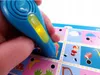 A hand holding a blue talking pen over a colorful learning game board with various images. Náhled obrázku produktu