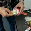 A person is using a yellow spatula to scoop white putty from a red container, with a can of putty and a tube of hardener on a black surface. Anteprima dell’immagine prodotto