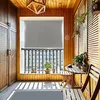 A balcony with wooden walls and floor, featuring a gray roller blind, a black metal railing, a small wooden table and chairs, and potted plants. Náhled obrázku produktu