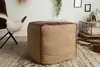 A cube-shaped ottoman with a leather top sits on a rug in a living room setting. A butterfly chair and a side table are visible in the background. Produktbild-Vorschau