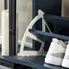 A close-up view of a shoe cabinet with white plastic supports and dark blue shelves, holding a pair of white and gray sneakers. Voir les images du produit