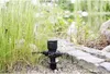 A black garden socket is placed in the ground next to tall grass and rocks, with a pond in the background. Produktbild-Vorschau