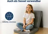 A young girl sits cross-legged on a folded mat, which is propped up like a chair. The background is a plain wall. Produktbild-Vorschau