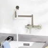 A wall-mounted kitchen faucet with water running into a sink. Podgląd zdjęcia produktu