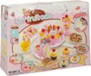 The image shows the packaging of a toy fruit cake cutting set. The packaging is pink and decorated with images of cakes, fruits, and a child playing with the toy. Podgląd zdjęcia produktu