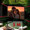 A projection screen is set up outdoors in a garden setting, displaying a romantic image of a couple. Red arrows indicate tensioning points. Voir les images du produit