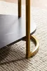Close-up of the leg and lower part of a marble-look coffee table with a gold metal frame, resting on a textured rug. Náhled obrázku produktu