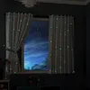 A bedroom window with curtains drawn, showing a starry night sky outside. The curtains have a glow-in-the-dark moon and star pattern. Produktbild-Vorschau