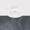 A white smoke detector is mounted on a white ceiling, with wisps of smoke visible below. Produktbild-Vorschau