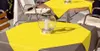 Two tables are set with yellow tablecloths and a glass lantern with a candle on each. Chairs are visible around the tables. Produktbild-Vorschau