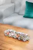 A Christmas advent candle holder decorated with pine cones, ornaments, and stars, placed on a wooden table in front of a white sofa. Náhled obrázku produktu