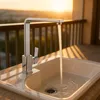 A modern kitchen faucet with water running into a sink, set against a sunset backdrop. Produktbild-Vorschau