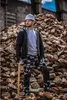 A construction worker in a hard hat and safety glasses stands in front of a large pile of rocks, holding a sledgehammer. Produktbild-Vorschau