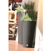 Two tall, dark rattan planters with plants are placed on a wooden deck next to a wall. A wooden chair and table are visible in the background. Produktbild-Vorschau