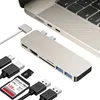 A silver USB-C hub is shown connected to a laptop, with various accessories like USB cables, an SD card, and a microSD card laid out around it. Produktbild-Vorschau