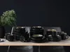 A collection of black stoneware dishes with gold and green accents, arranged on a wooden table with a sprig of greenery in a vase. Náhľad obrázku produktu