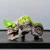 A toy chameleon creature with green horns and a spiky green back, standing on a dark surface against a light gray background. Produktbild-Vorschau