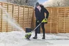 A person is using a snow blower to clear snow from a patio area in a backyard. Produktbild-Vorschau