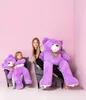 A woman and a child are sitting in chairs with large purple teddy bears. Produktbild-Vorschau