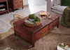 A wooden coffee table with drawers is placed on a rug in a living room setting, with a sofa visible in the background. Produktbild-Vorschau